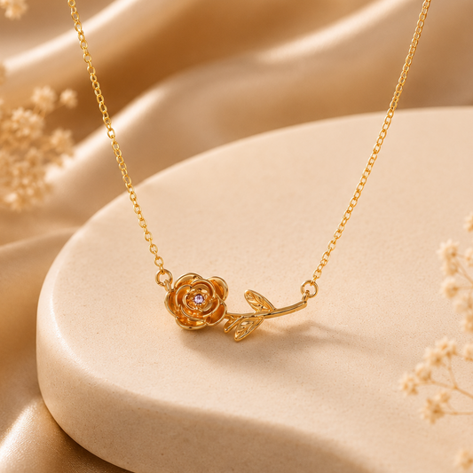 Gold necklace with a rose pendant on a beige stone surface with dried flowers.