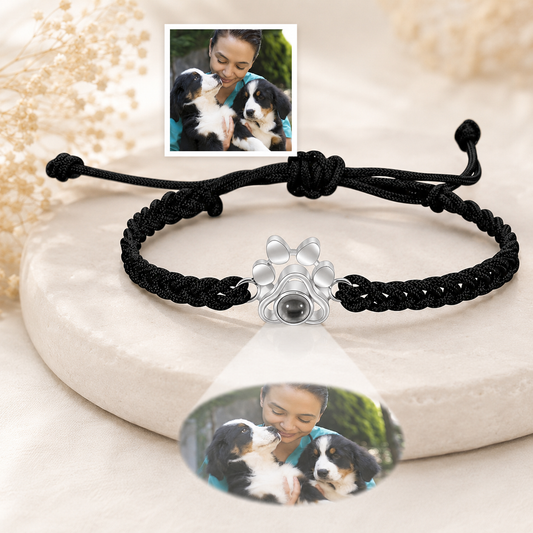 Black braided projection bracelet with a paw-shaped charm featuring a photo of a woman with two dogs on a white stone surface.