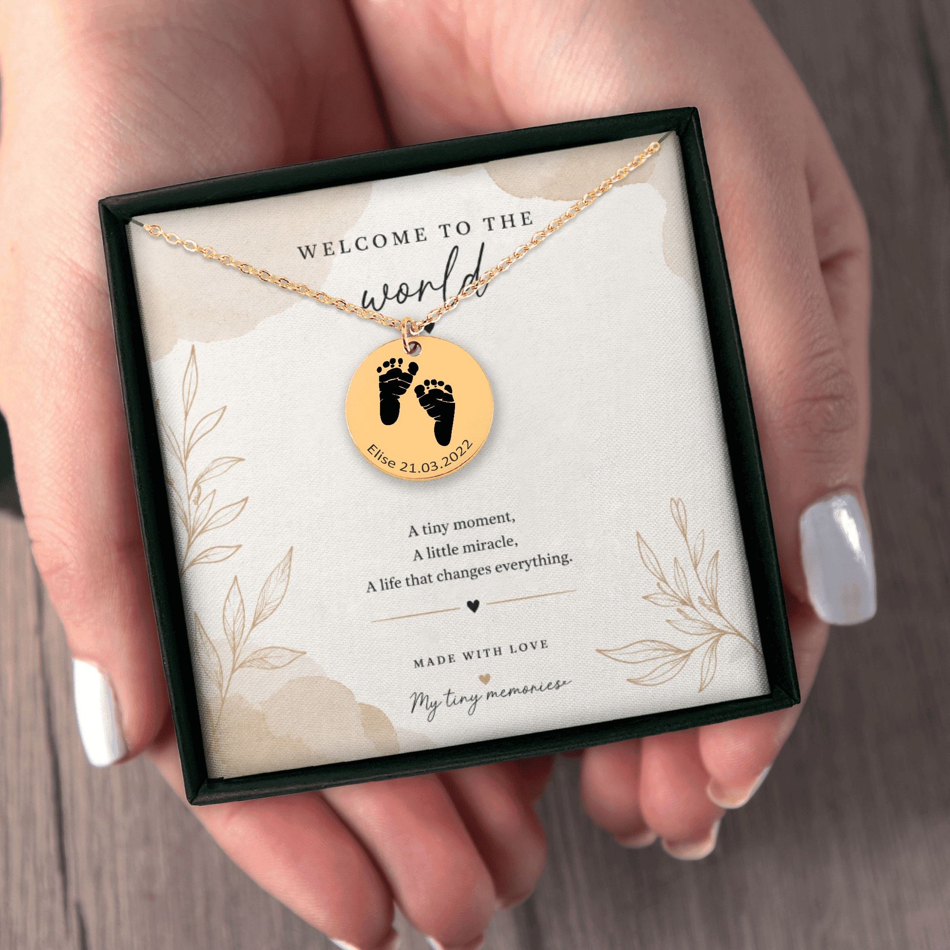 Necklace with a gold pendant featuring footprints in a jewelry box with a message card.