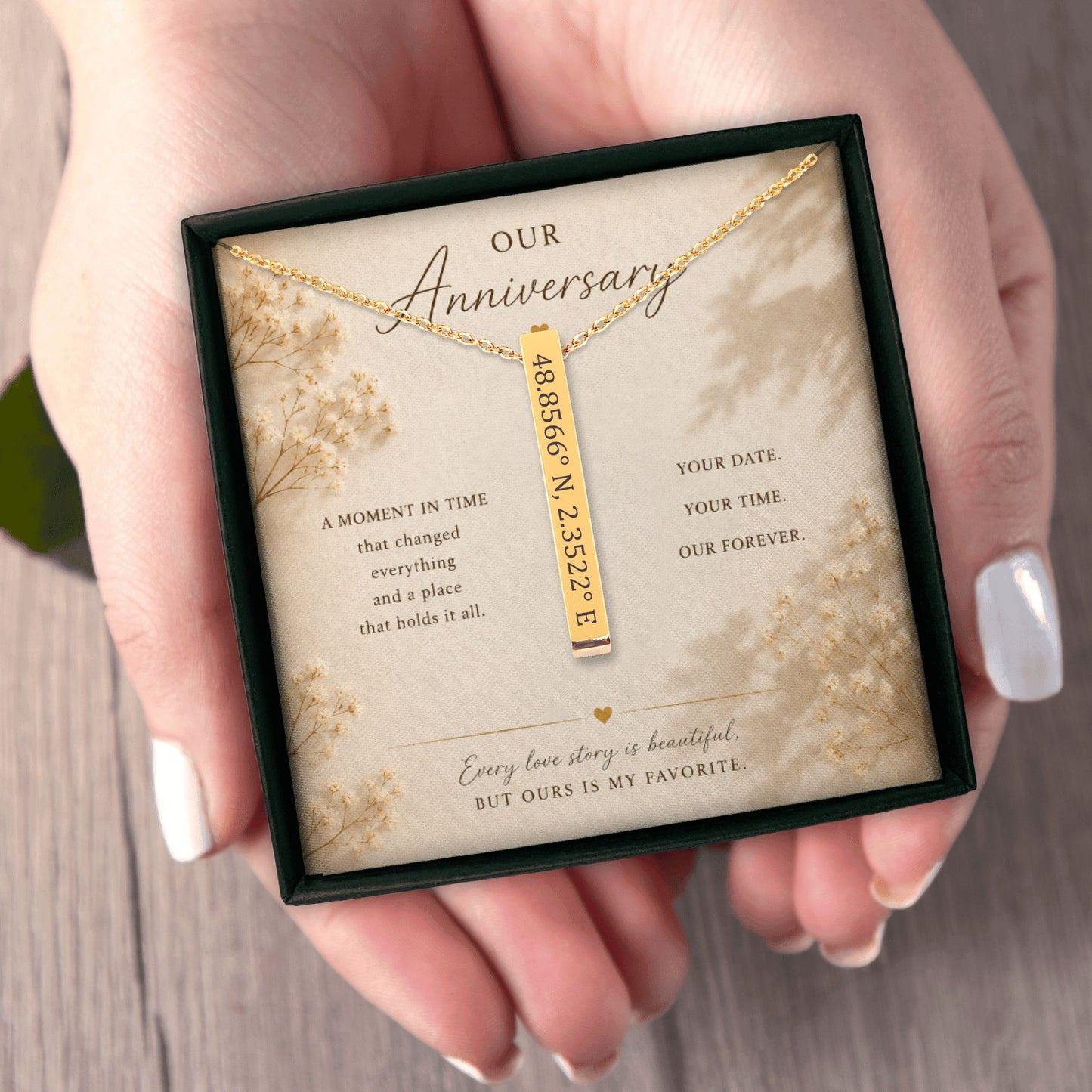 Gold necklace with engraved coordinates in a decorative box held by hands.