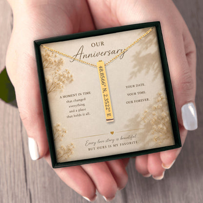 Gold necklace with engraved coordinates in a decorative box held by hands.