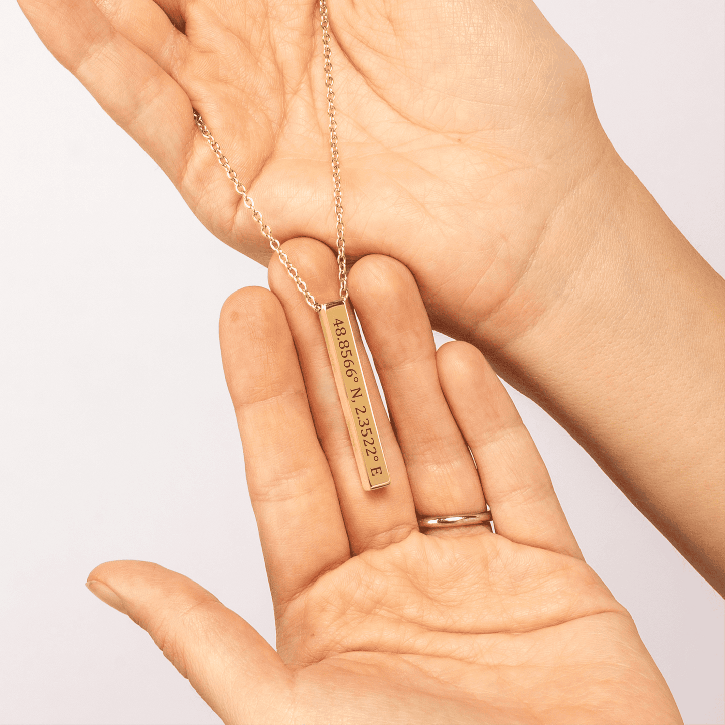 Gold necklace with coordinates pendant held in a hand against a light background