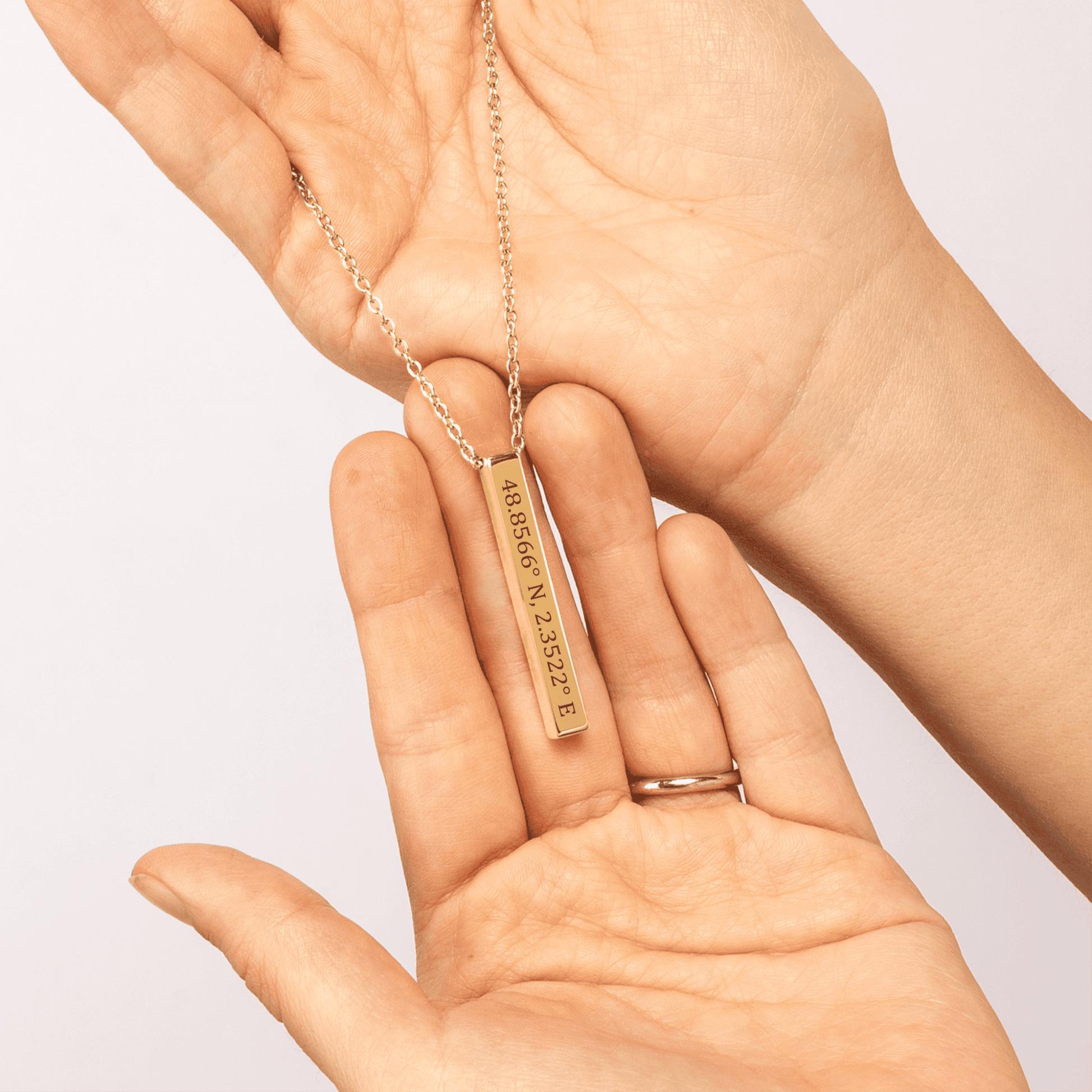 Gold necklace with coordinates pendant held in a hand against a light background