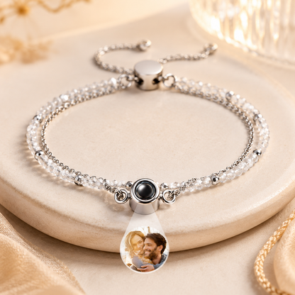 Silver bracelet with a teardrop-shaped charm featuring an engraved image on a beige surface.