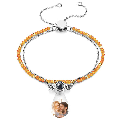 Bracelet with orange beads and a teardrop-shaped charm featuring a photo of a couple.