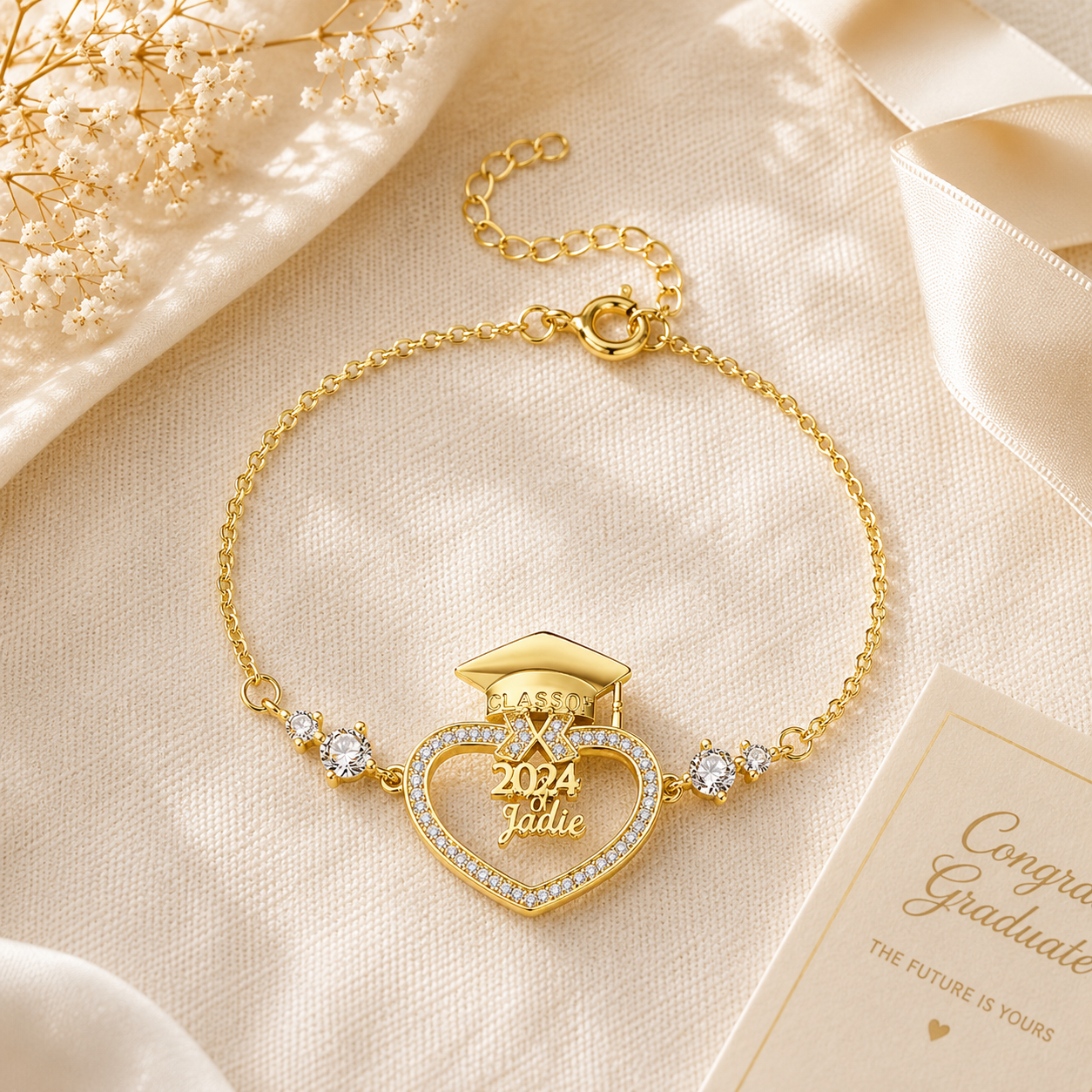 Gold bracelet with heart design and '2024 Graduate' text on a beige fabric background
