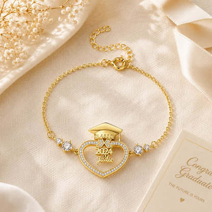 Gold bracelet with heart design and '2024 Graduate' text on a beige fabric background