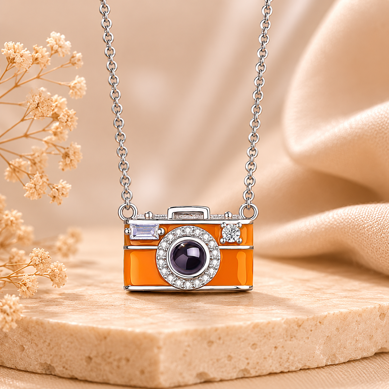 Orange camera-shaped projection pendant with decorative elements on a chain, set against a beige background.