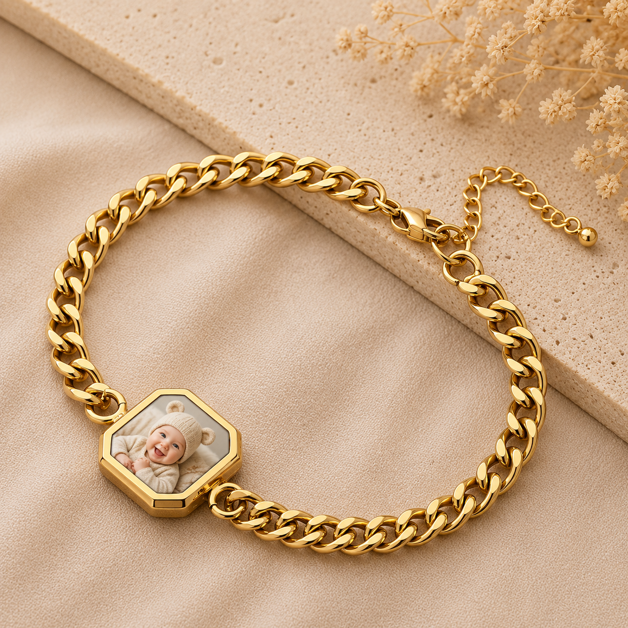 Gold chain bracelet with a hexagonal charm featuring a baby's photo on a beige surface.