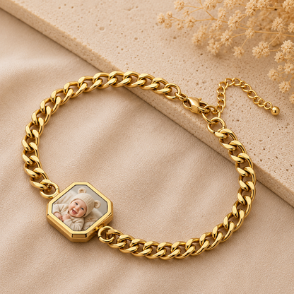 Gold chain bracelet with a hexagonal charm featuring a baby's photo on a beige surface.