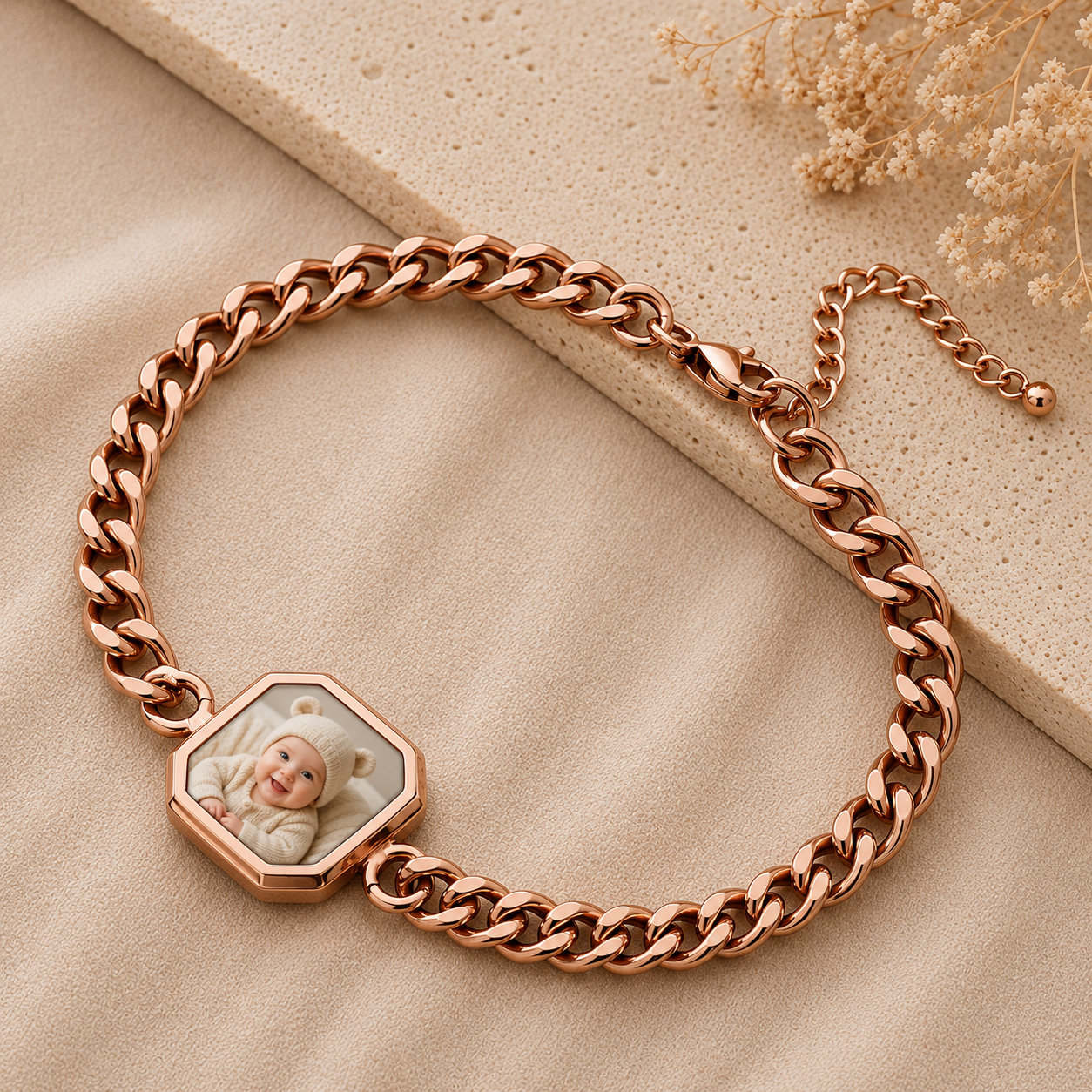 Rose gold chain bracelet with a hexagonal charm featuring a baby's photo on a beige surface.