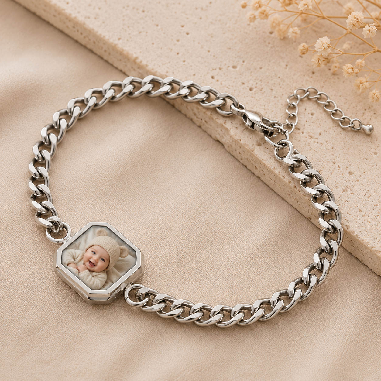 Silver chain bracelet with a hexagonal photo charm on a beige surface with dried flowers.