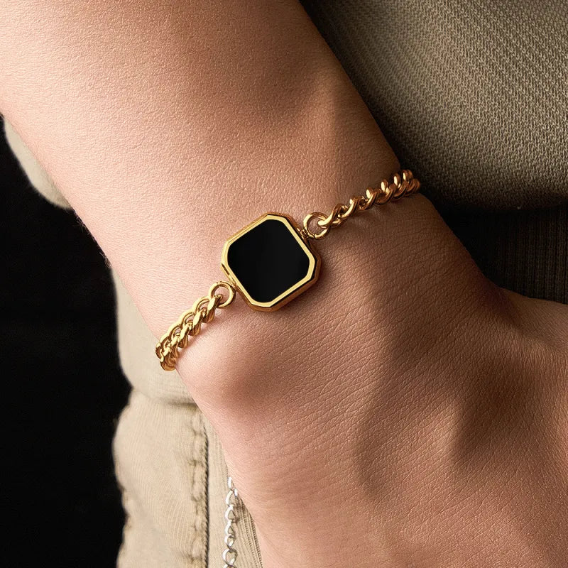 Gold bracelet with a black hexagonal stone on a wrist.