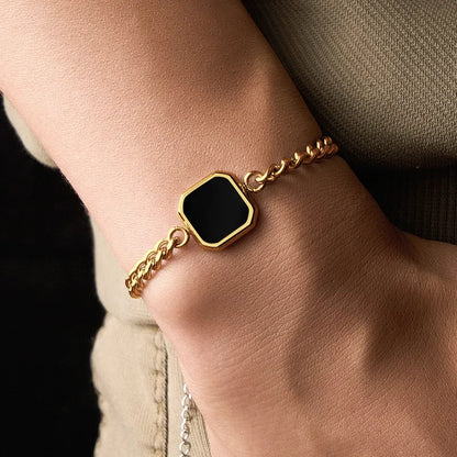 Gold bracelet with a black hexagonal stone on a wrist.