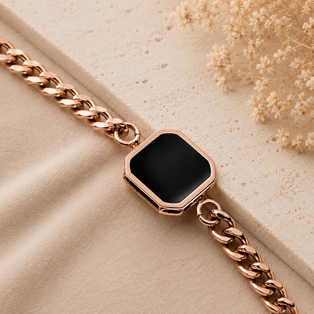 Rose gold bracelet with a black hexagonal stone on a beige surface with dried flowers.