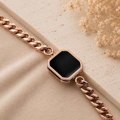 Rose gold bracelet with a black hexagonal stone on a beige surface with dried flowers.