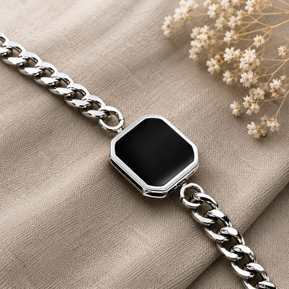 Silver chain bracelet with a black square pendant on a beige fabric background