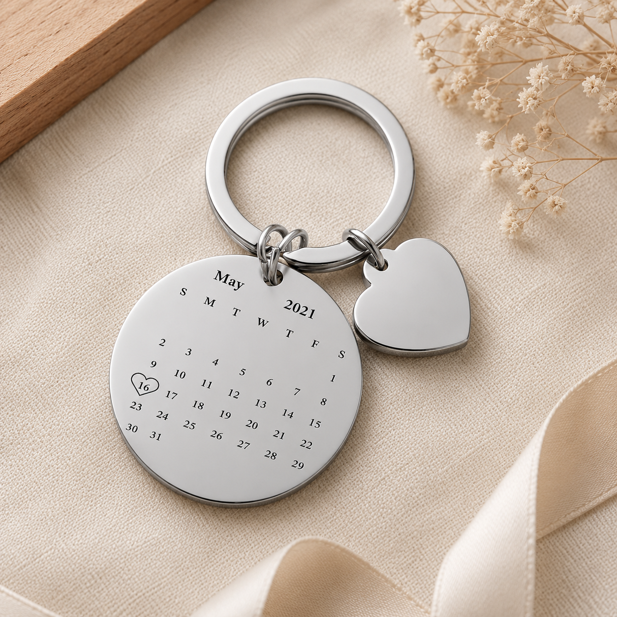 Silver keychain with calendar tag and heart charm on a beige surface