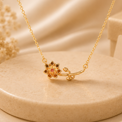 Gold necklace with floral design on a beige surface with gift box and flowers.