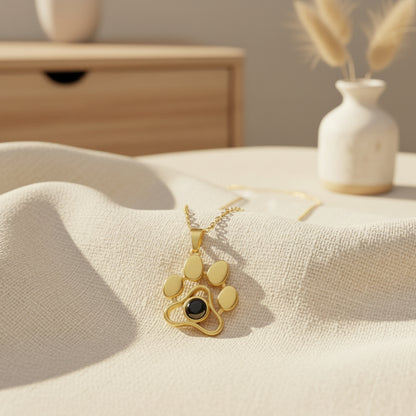 Gold paw-shaped necklace with a black gemstone on a beige fabric surface.