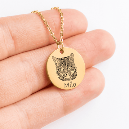 Gold necklace with a cat pendant and engraved name 'Milo' held in a hand.