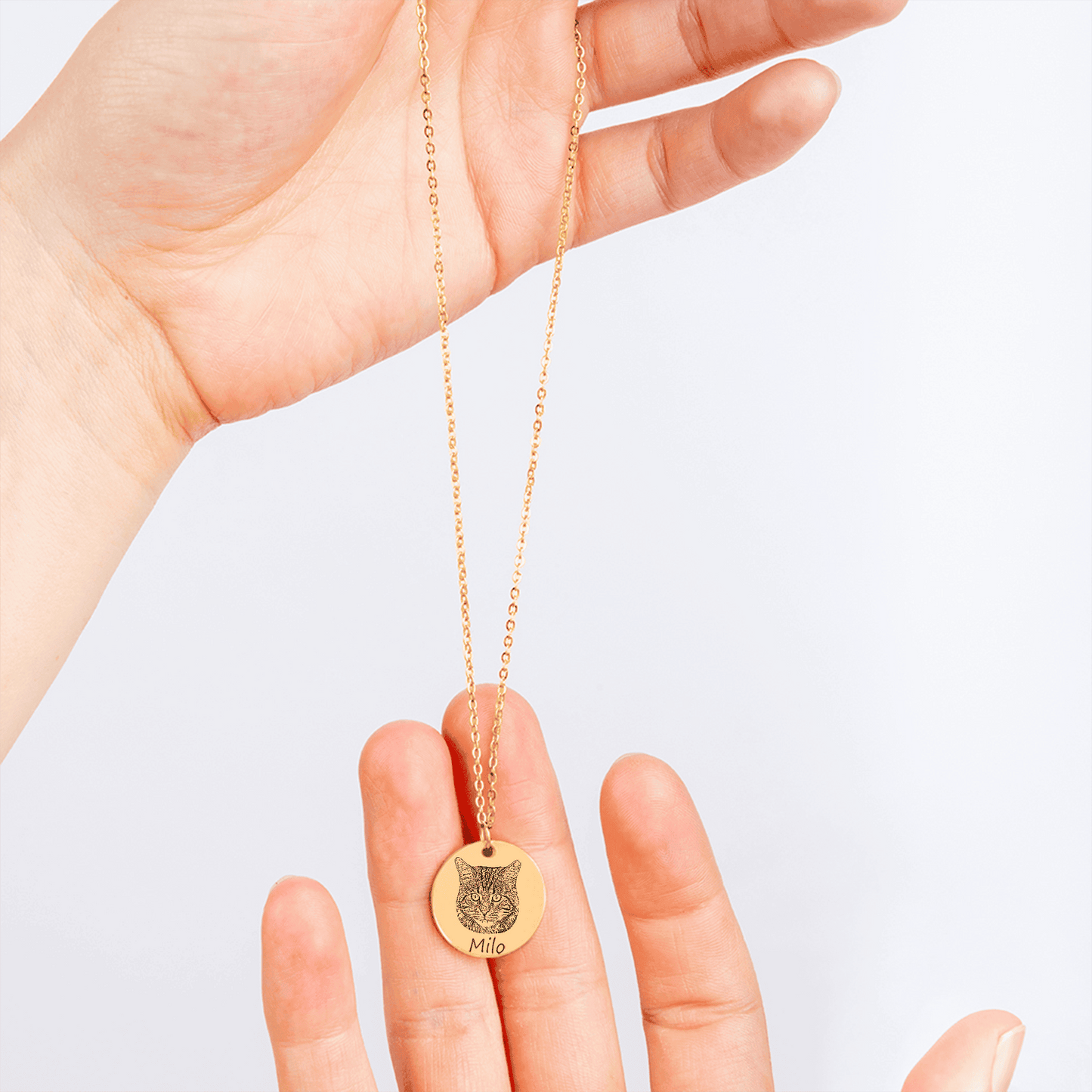 Gold necklace with a cat pendant held by a hand on a light background